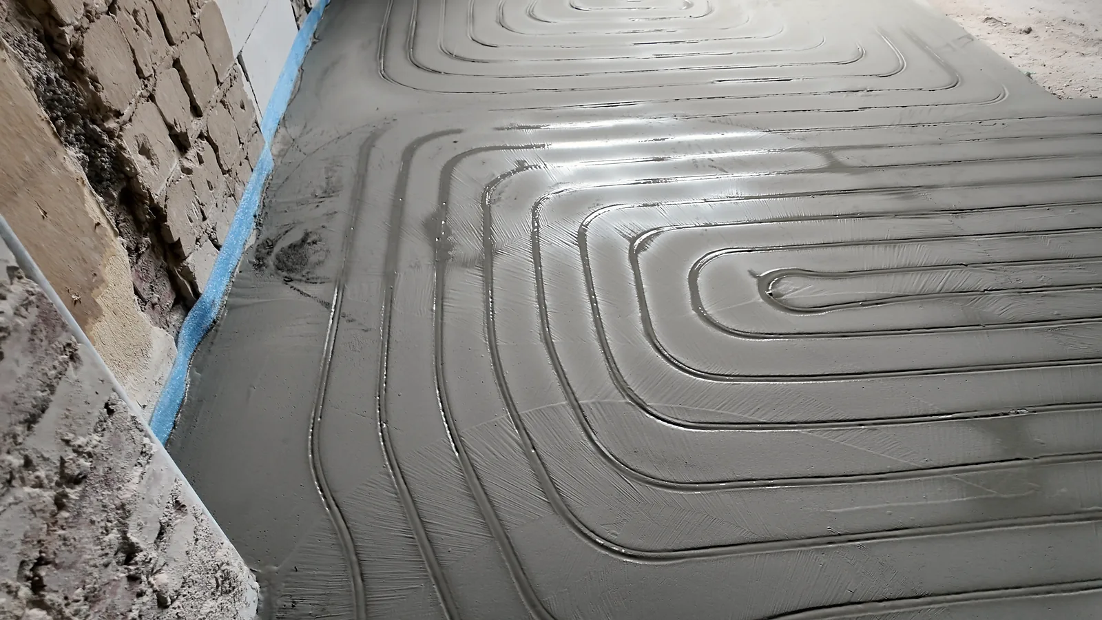 Frisch verfüllte Kanäle in Spiralform auf dem Boden, am Wandrand ein blauer Dämmstreifen