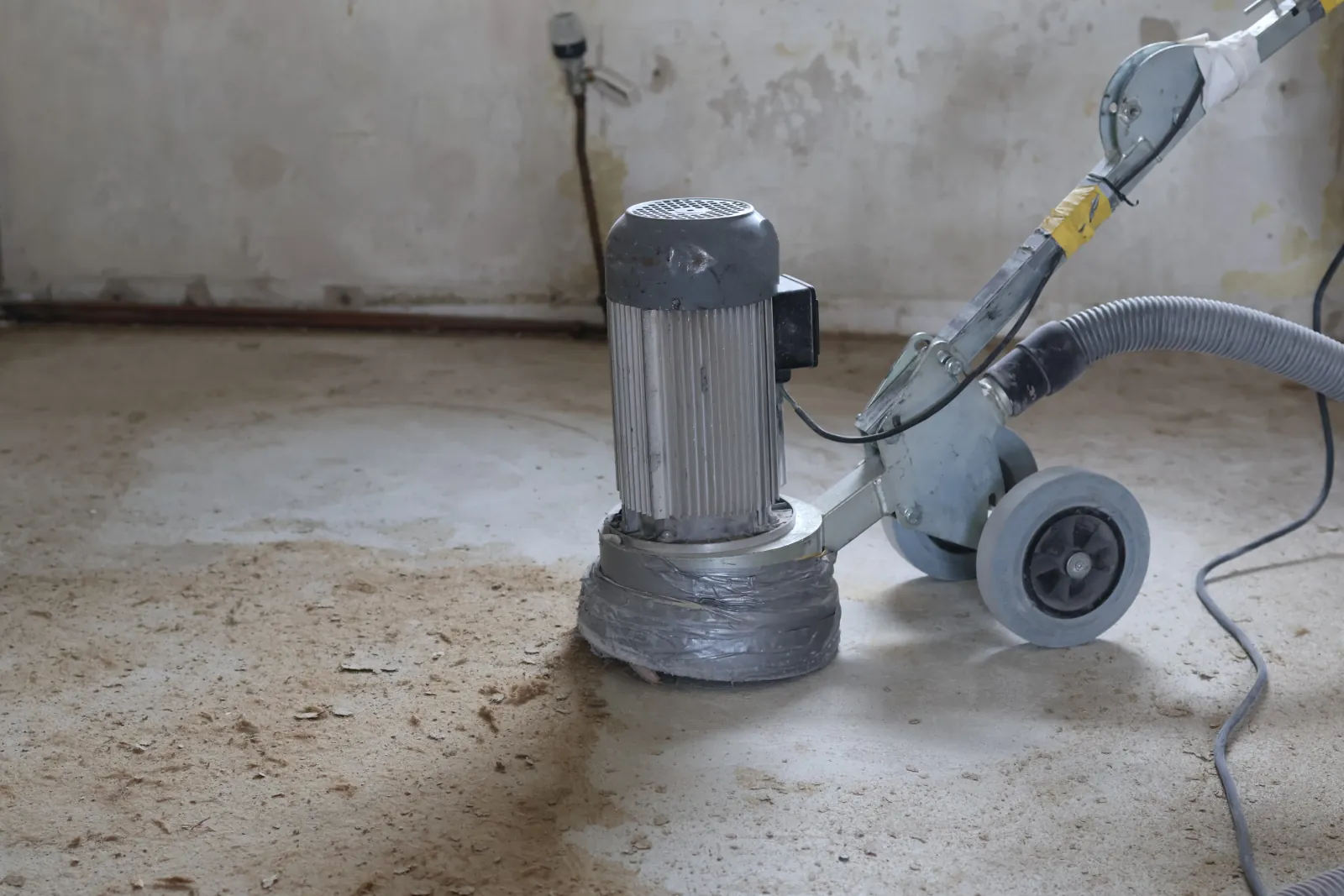 Schleifmaschine mit Absaugschlauch auf dem Estrich, im Hintergrund eine alte Wand