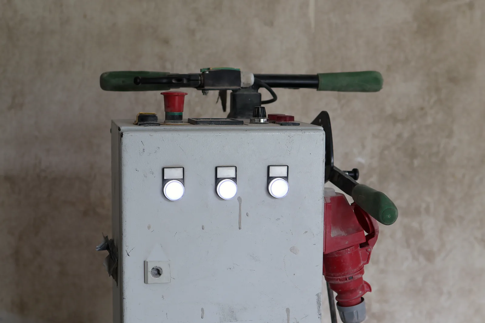 Grauer Schaltkasten einer Fräsmaschine mit drei Leuchtknöpfen und einem roten Drehstromstecker an der Seite