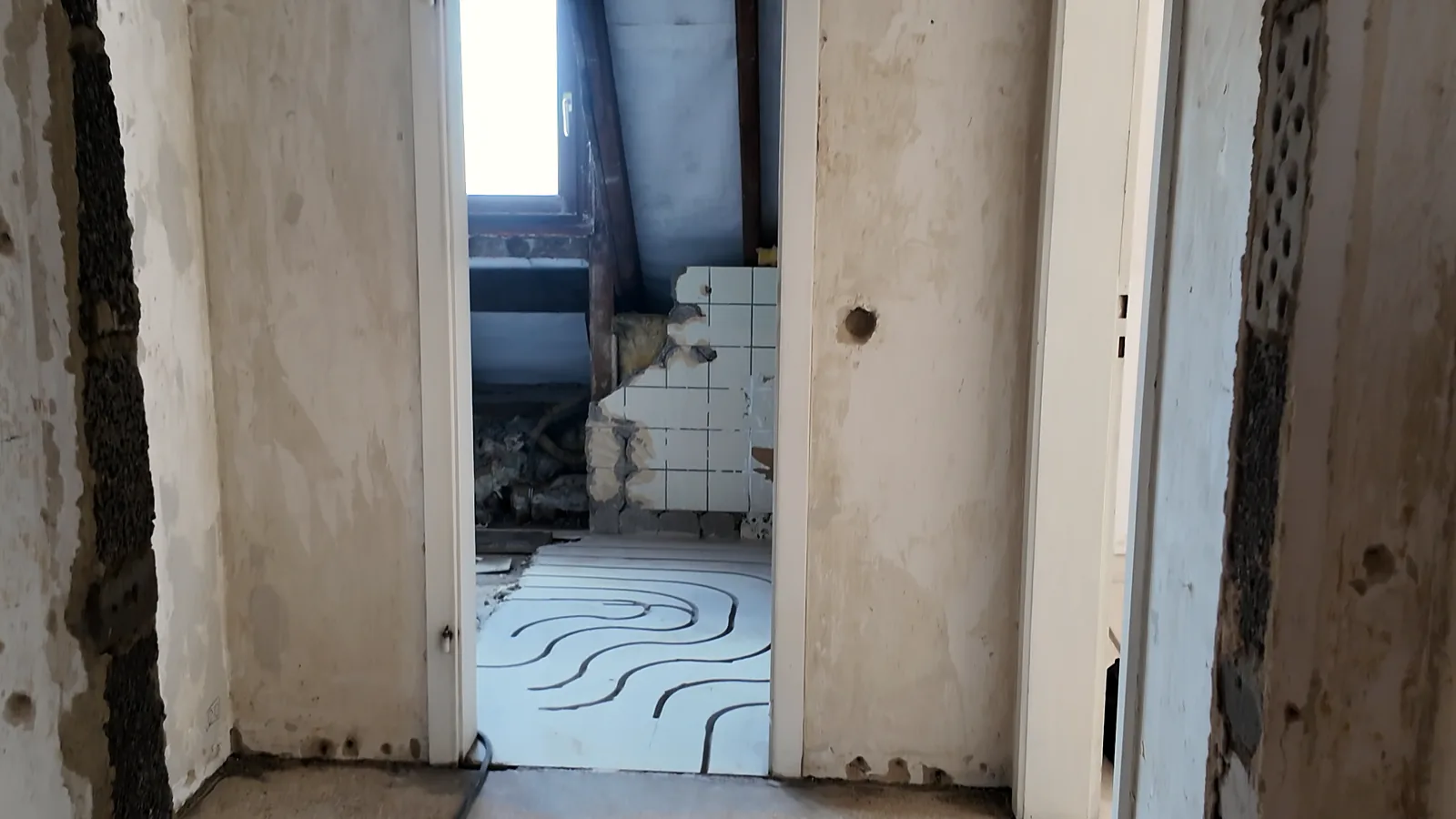 Blick durch einen Durchgang in einen Raum mit gefrästen Kanälen, im Hintergrund Fliesen an der Wand