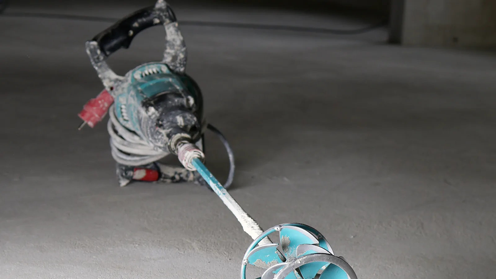 Handrührwerk mit Mörtelresten und aufgewickeltem Kabel steht auf dem Boden eines Raums