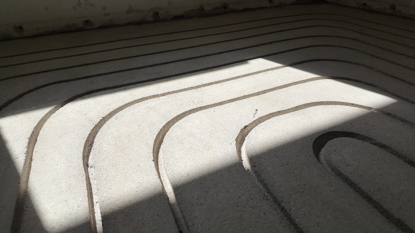 Gefräste Kanäle in einem Estrich, ein Streifen Sonnenlicht fällt von links auf die Bögen
