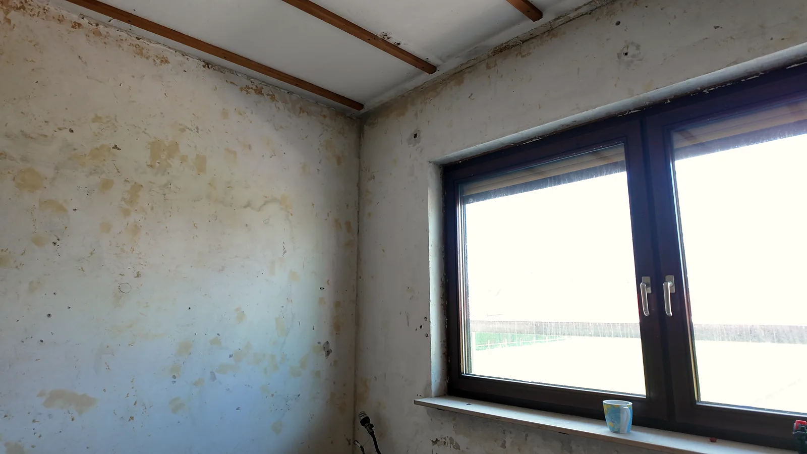 Leerer Altbauraum mit Fenster und Dachschräge, auf der Fensterbank steht eine Tasse