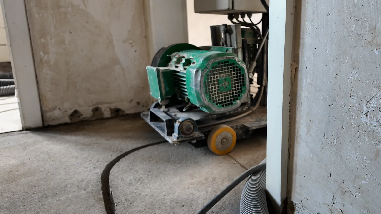 Fräsmaschine mit grünem Motor in einer Raumecke, davor ein gefräster Kanal, rechts ein Türrahmen