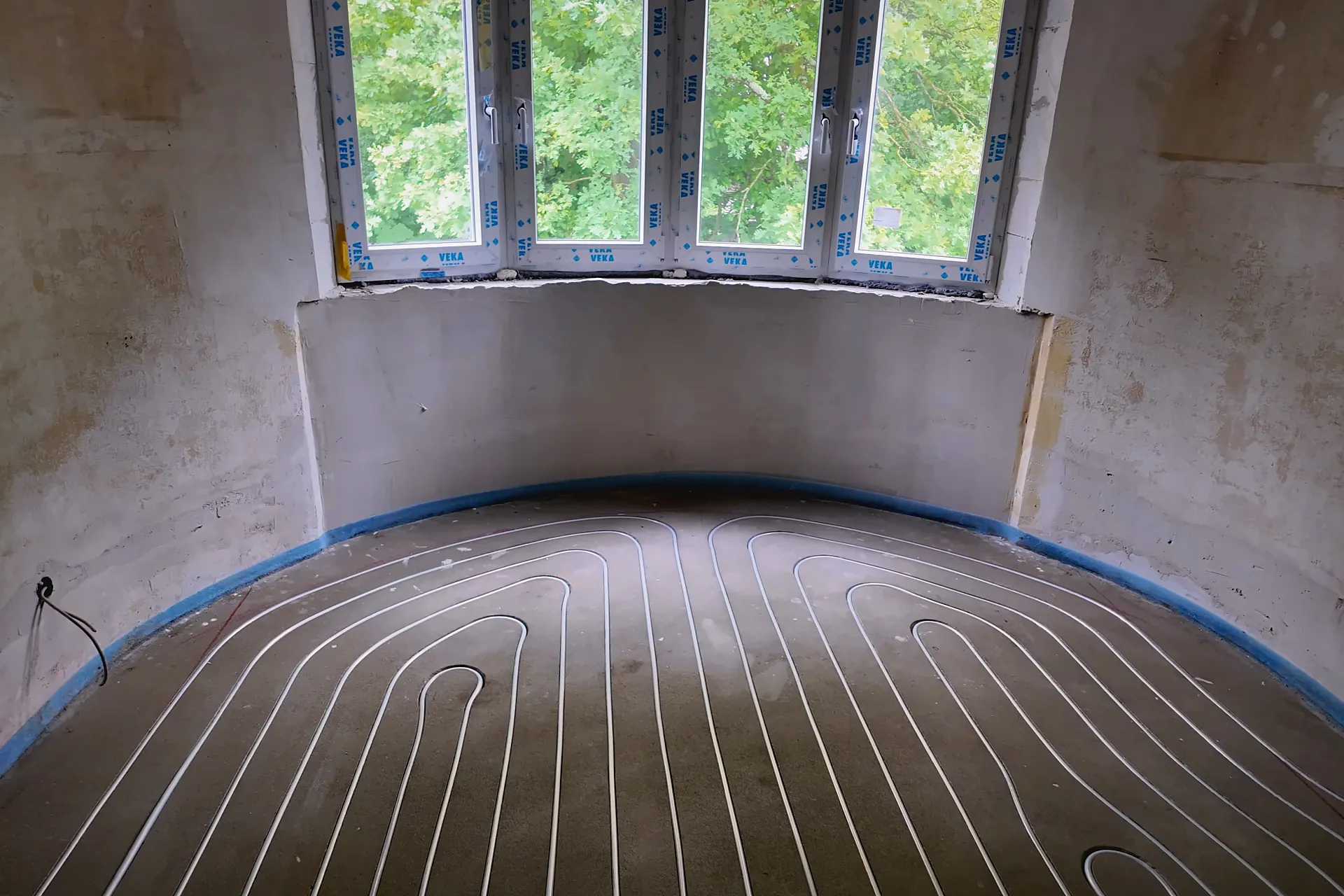 Erkerraum mit eingelegten Heizrohren in den Kanälen, im Hintergrund eine Fensterfront mit Grün
