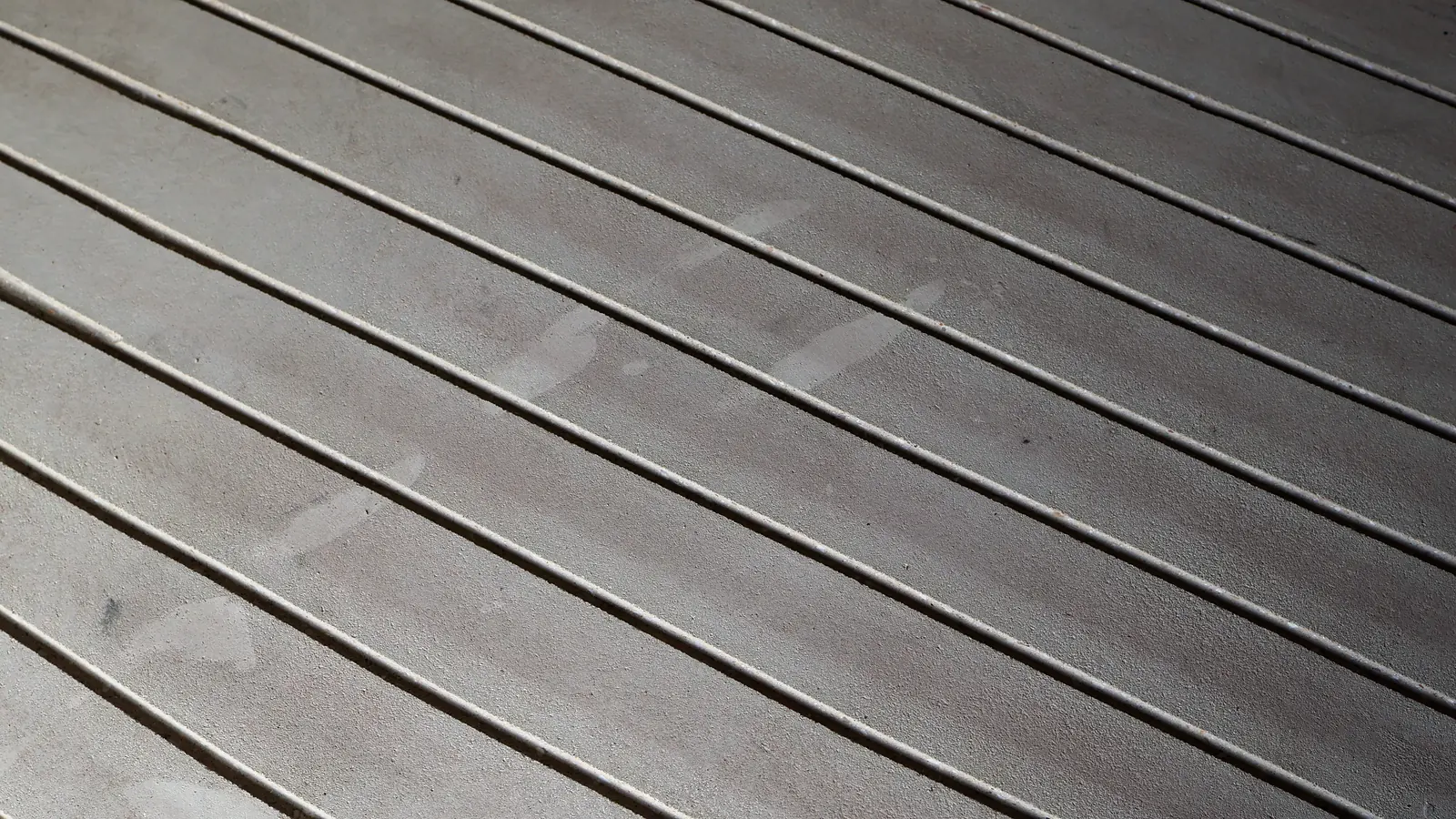 Gefräste, leere Kanäle in hellem Estrich, die diagonal durchs Bild laufen