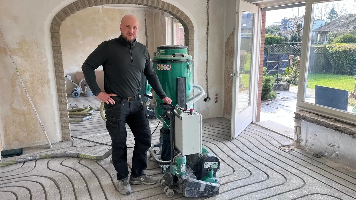 Kamil Bregulla im Altbau vor dem Rundbogen, im Estrich die gefrästen Kanäle für die Fußbodenheizung