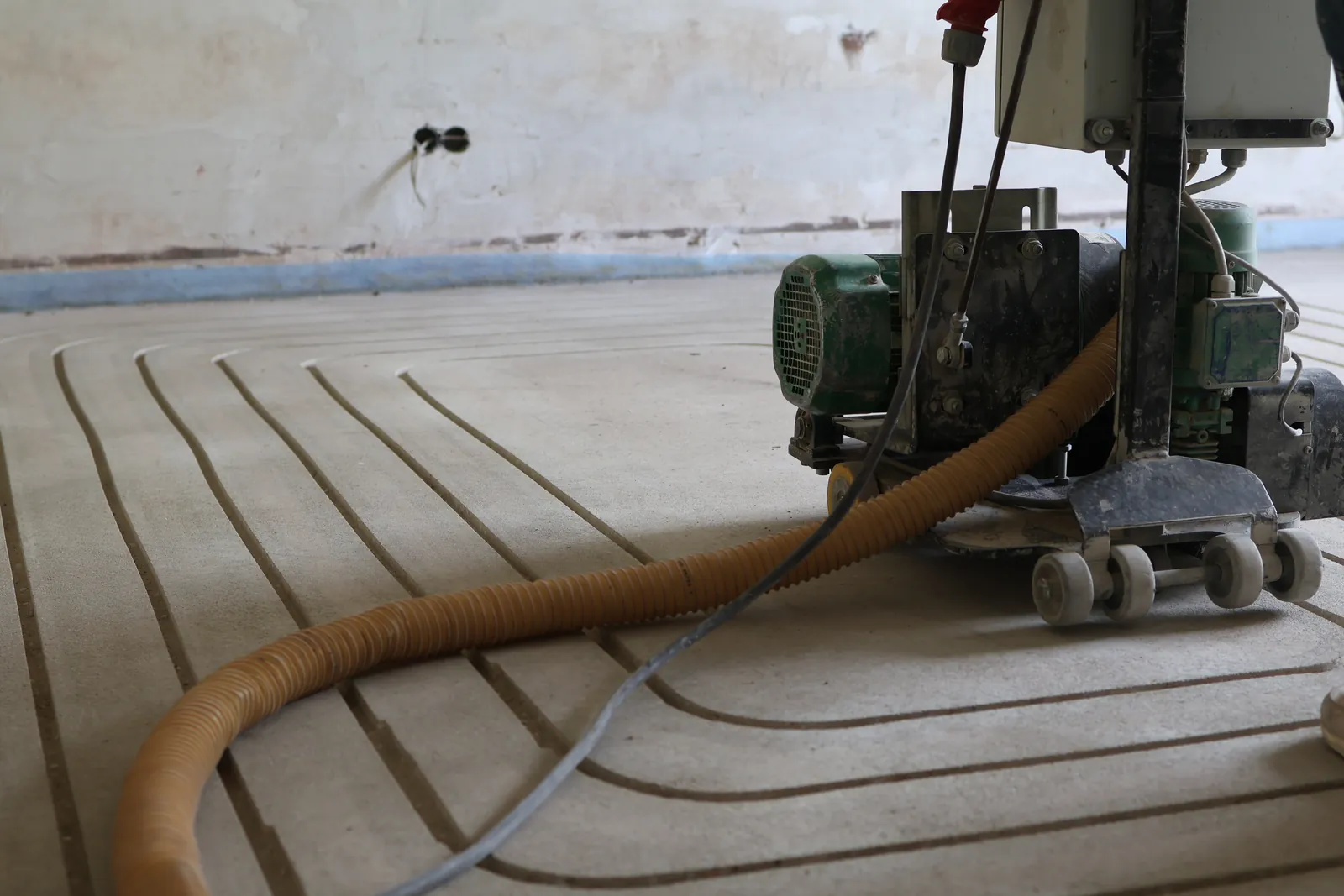 Fräsmaschine mit Absaugschlauch im Raum, davor die gefrästen Kanäle für die Fußbodenheizung im Estrich